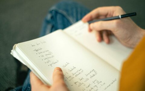 Close-up of a person taking notes in a notebook, writing a to-do list with a pencil.