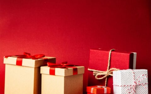 A collection of colorful gift boxes with ribbons on a rich red background, perfect for holiday themes.