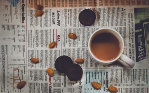 A cozy setup with coffee, cookies, and almonds on a newspaper, perfect for breakfast vibes.