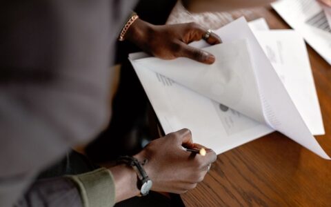 African American adult revising papers with a pencil at a desk, focus on hands and documents.