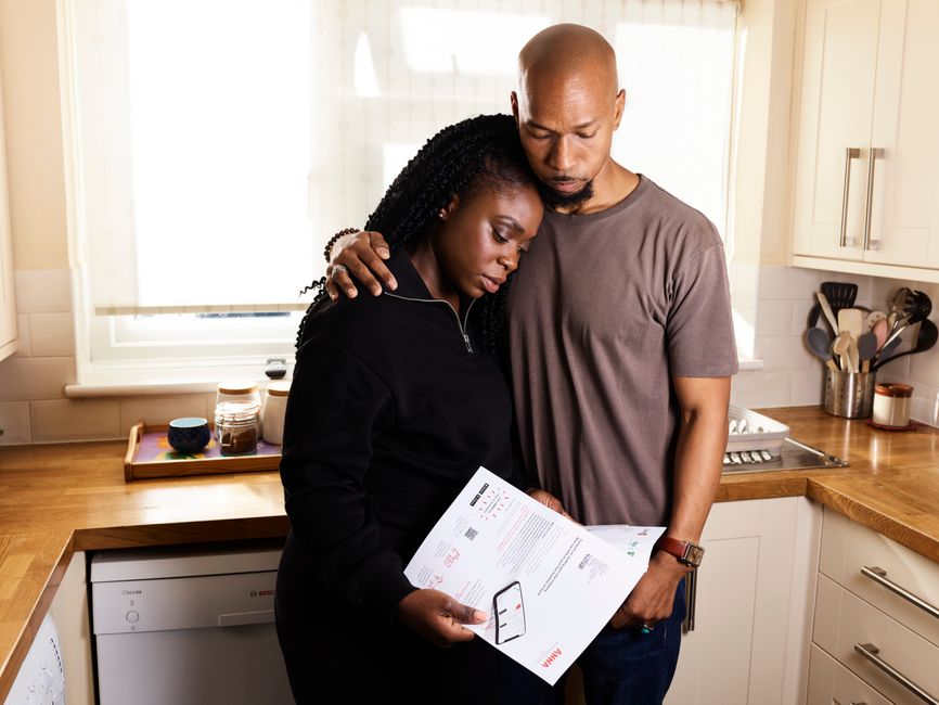 A couple embraces in their kitchen while going through important documents, reflecting concern and support.