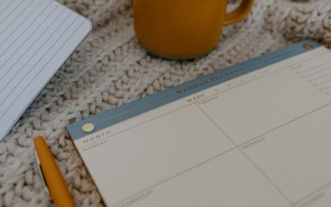A cozy workspace featuring a weekly planner, pen, and coffee mug on knitted fabric. Perfect for planning.